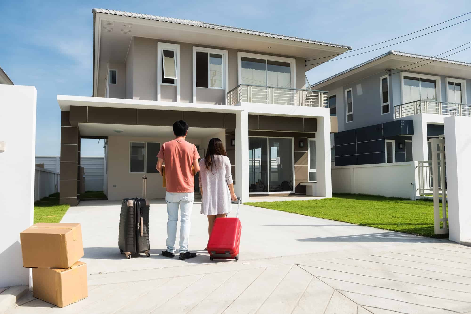 Husband and wife standing in front of new buying home with luggage and  boxes. Happy Asian married male and female couple move to modern house. Family lifestyle new life. They bought first home